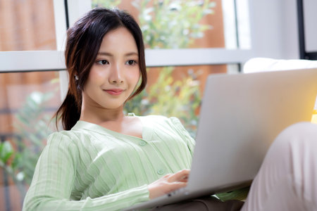 Young asian business woman working with laptop sitting on sofa in home office, businesswoman using on notebook in living room at home, woman relax with using laptop to social online, business concept.の写真素材