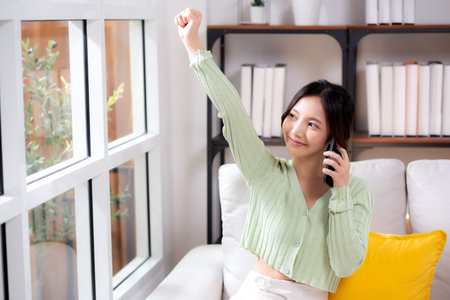 Young asian businesswoman telephone smiling and relax sitting on sofa in living room at home, cheerful woman talking with smart phone sitting on couch in home, lifestyle and communication.の写真素材