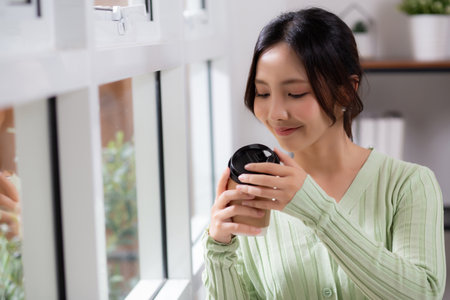 Portrait young asian woman relax with smell and drinking coffee by the window in living room at home, woman smiling with happiness and comfortable drinking beverage, lifestyle and leisure.の写真素材