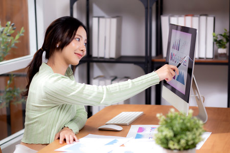 Young asian businesswoman planning and strategy about finance looking graph and chart of report marketing in home office, business woman analyzing financial and revenue for success, business concept.の写真素材