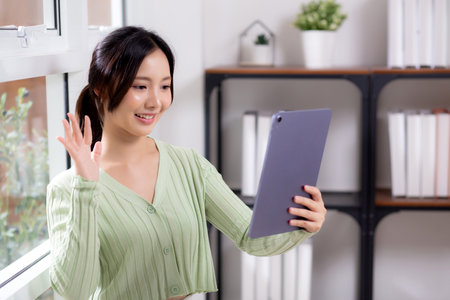Portrait young asian business woman using digital tablet computer for video call by the window in living room at home office, businesswoman and expression while video call, lifestyle and business.の写真素材