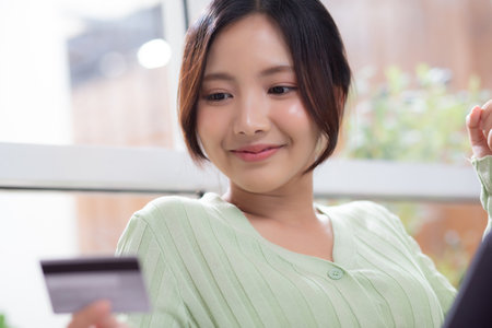 Young asian woman sitting on sofa using tablet computer shopping online with credit card buying to internet while cheerful, female payment with business, purchase and payment, business and finance.の写真素材