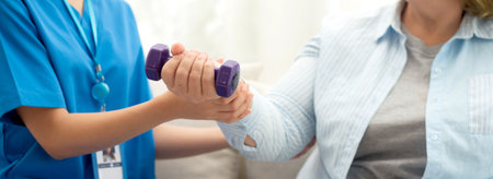 Asian caregiver woman or nurse training senior woman lifting dumbbell for arm exercise while therapy and rehabilitation in living room at home, caretaker or physiotherapist helping elderly workout.の写真素材