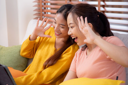 Two young asian woman sitting on sofa using digital tablet for video call in living room at home, female using social media on tablet for online and conversation distant, lifestyles concept.の写真素材