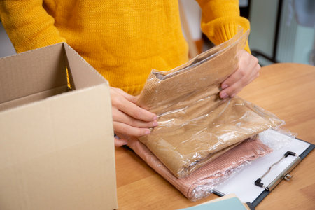 Closeup hand of woman packing in cardboard box for shipping or storage in home office, online seller packing clothes in box for delivery, logistic and cargo, service of retail.の写真素材