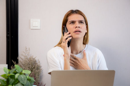 Young caucasian businesswoman working on laptop computer while talking on smartphone with stress and upset in office, business woman talking on smart phone with frustrated, business and expression.の写真素材