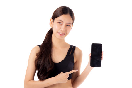 Young asian woman in sportswear workout holding and presenting blank screen smartphone isolated white background, girl in sportswear showing mockup smart phone, sport and health care concept.の写真素材
