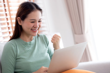 Young asian business woman working with laptop sitting on sofa in home office, businesswoman using on notebook in living room at home, woman relax with using laptop while success, business concept.の写真素材