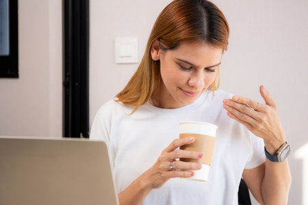 Happiness young caucasian businesswoman drinking coffee while working on laptop computer in home office, happy business woman drinking beverage while using laptop for relax, business concept.の写真素材