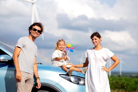 Happy family by a car with wind turbines, happiness family and bonding, recreation and renewable with innovation, windmill with resource sustainable power, travel in vacation and environmental.の写真素材