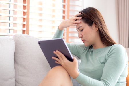 Young asian business woman using tablet computer stress and worried sitting on sofa in living room at home office, businesswoman working on tablet while concerned and tire, business and lifestyle.の写真素材