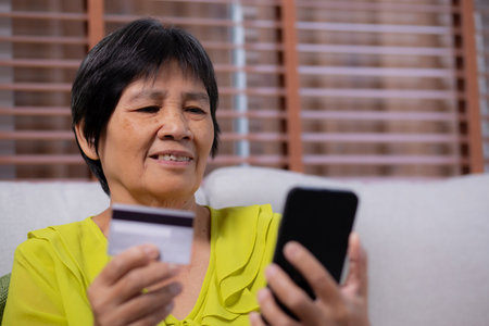 Senior asian woman sitting on sofa using smart phone shopping online with credit card buying to internet, female payment with business with smartphone, purchase and payment, business and finance.の写真素材