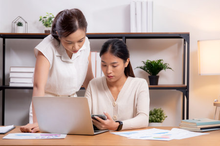 Two young asian businesswoman planning and strategy about marketing and financial with colleagues looking laptop and tablet, meeting and working on laptop with partner, business and consulting.の写真素材