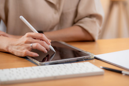 Closeup hand young businesswoman using tablet while writing on desk in living room at modern home office, business woman using tablet, entrepreneur or freelance, business and commercial.の写真素材