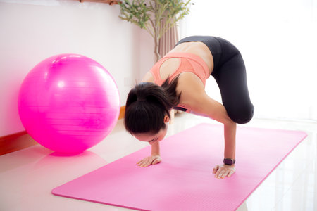 Young asian woman in activewear practicing yoga on mat in living room at home, woman practicing workout with strength and strong of arm and hand, sport for flexibility and wellness, one person.の写真素材