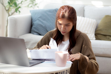 Young asian woman calculates bills finance and cost in living room at home, woman looking expense with burden or investment on paperwork, statement banking and debt for loan, business and financial.の写真素材