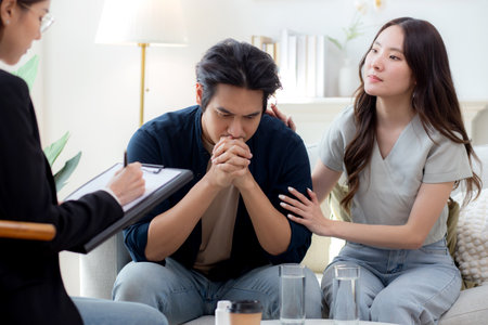 Young asian couple experiencing marriage counseling, wife comforting partner while talking with psychologist for mental health and consultation, examining health with anxious, medical and couple.の写真素材