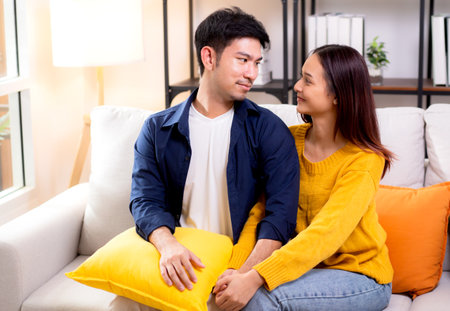 Portrait young asian couple hold hands sitting on sofa looking affectionate and embrace in living room at home, husband and wife with gentle and relation with cozy and love, couple and lifestyle.の写真素材