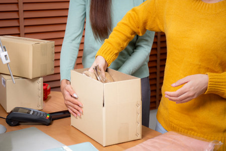Closeup hand of woman packing in cardboard box for shipping or storage in home office, online seller packing clothes in box for delivery, logistic and cargo, service of retail.の写真素材