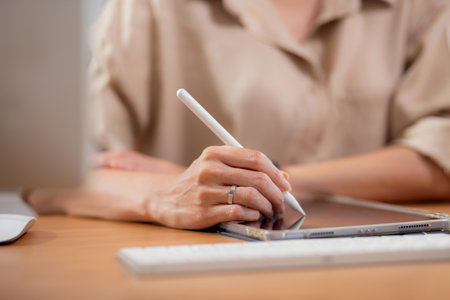 Closeup hand young businesswoman using tablet while writing on desk in living room at modern home office, business woman using tablet, entrepreneur or freelance, business and commercial.の写真素材