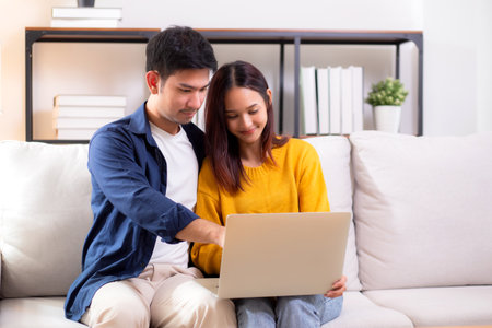 Young asian couple looking on laptop for relax with cozy and contentment sitting on sofa in living room at home, couple leisure watching laptop on couch, relationship and bonding, lifestyle concept.の写真素材