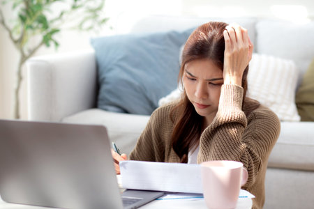 Young asian woman checking document about finance with stress and worried in living room at home, woman looking bill financial about debt and expenses with anxiety, business and finance.の写真素材