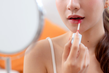 Closeup hands beauty young asian woman applying makeup with lipstick looking mirror in living room at home, beauty woman applying make-up with cosmetic on facial for glamour, make up and cosmetic.の写真素材