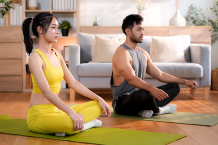 Young asian couple practicing yoga and meditation together in the living room at home, relaxation, wellness and healthy lifestyle, calm and enjoying mindful tranquility with yoga, sport for health.の写真素材