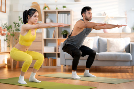 Fitness coach guidance with asian woman during squat training at home in living room, workout and exercise for healthy lifestyle, instructor and body strength coaching, practice stretching of muscle.の写真素材