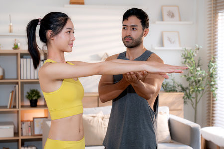 Fitness coach guidance with asian woman during squat training at home in living room, workout and exercise for healthy lifestyle, instructor and body strength coaching, practice stretching of muscle.の写真素材