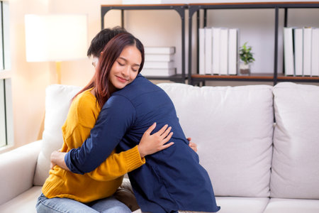 Young asian couple hug sitting on sofa with affectionate in living room at home, husband and wife with gentle and relation with cozy and love while embrace, bonding and comfort, couple and lifestyle.の写真素材