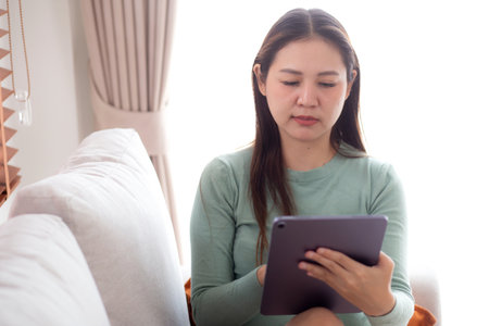 Young asian business woman using tablet computer for relax and check social media online sitting on sofa in living room at home office, businesswoman working on tablet with device, business concept.の写真素材