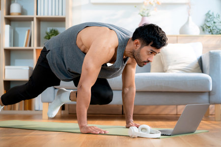 Young asian man doing home workout while watching online tutorial on laptop computer in living room at home, determined and motivation for health, healthy lifestyle and body strength for exercise.の写真素材