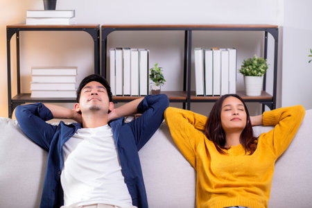 Young asian couple relaxing together on a comfortable sofa at home in the living room, happy and peaceful moment representing love, relationship and modern lifestyle of couple while sitting on couch.の写真素材