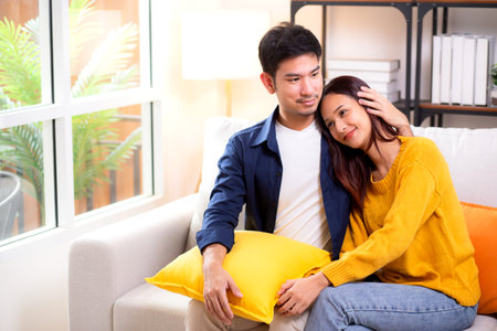 Portrait young asian couple hold hands sitting on sofa looking affectionate and embrace in living room at home, husband and wife with gentle and relation with cozy and love, couple and lifestyle.の写真素材