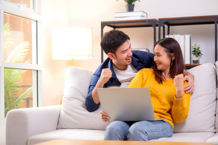 Young asian couple looking on laptop for relax with cozy and success sitting on sofa in living room at home, couple leisure watching laptop on couch, relationship and bonding, lifestyle concept.の写真素材