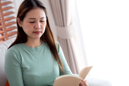 Young asian woman reading a book with expression sitting on sofa in living room at home, woman relax and leisure sitting on couch reading literature, activity and hobby, lifestyle and relaxation.の写真素材