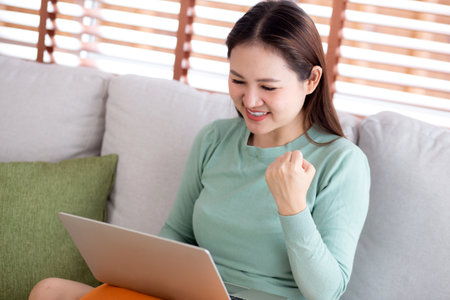 Young asian business woman working with laptop sitting on sofa in home office, businesswoman using on notebook in living room at home, woman relax with using laptop while success, business concept.の写真素材
