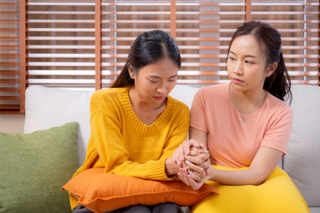 Young asian woman comforting friend with crying and depression sitting on sofa in living room, distress and empathy with friendship, hopelessness and mental health while woman encourage friend.の写真素材