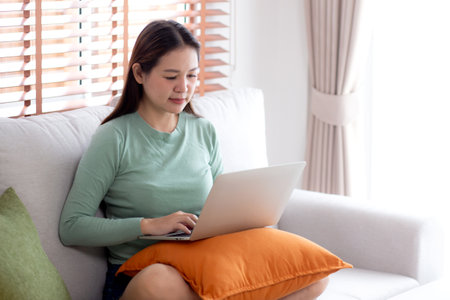 Portrait young asian business woman sitting on sofa using laptop computer in living room at home, businesswoman sitting on couch working on notebook with comfortable, business and freelance.の写真素材