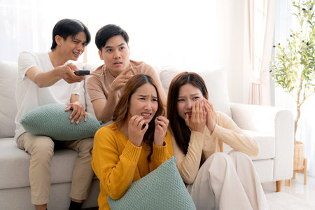 Group asian friends watching a horror movie at home with reaction with fear and surprise sitting on...