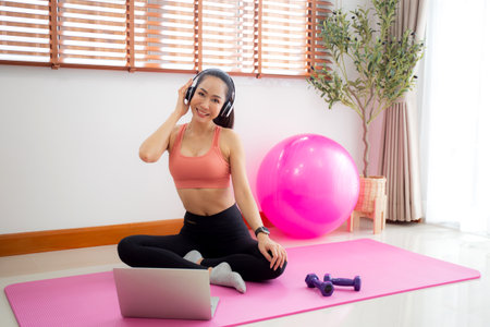 Young asian woman watch laptop after practice yoga and workout and listening music on headphone in living room at home, woman using notebook and listen music after exercise, sport and wellbeing.の写真素材