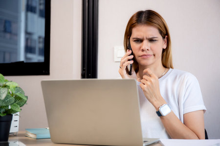 Young caucasian businesswoman working on laptop computer while talking on smartphone with stress and upset in office, business woman talking on smart phone with frustrated, business and expression.の写真素材