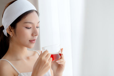 Beautiful young asian woman with headband enjoying tea standing near window with satisfied in living room at home, happy woman drinking tea or beverage for health and relaxation, lifestyle and health.の写真素材