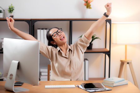 Young asian business woman using desktop computer for success in modern home office, businesswoman working with desktop computer while winning and satisfied in living room at home, business concept.の写真素材