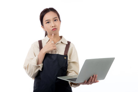 Portrait young asian business woman wearing apron holding laptop computer isolated white background, waitress or barista holding laptop computer while thoughtful, cut out, business or freelance.の写真素材