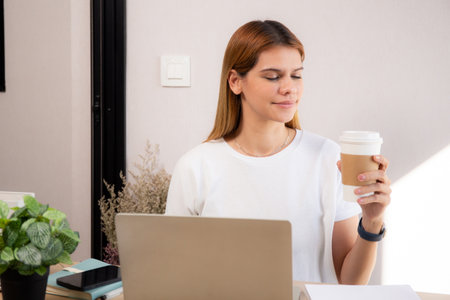Happiness young caucasian businesswoman drinking coffee while working on laptop computer in home office, happy business woman drinking beverage while using laptop for relax, business concept.の写真素材