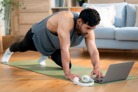 Young asian man doing home workout while watching online tutorial on laptop computer in living room at home, determined and motivation for health, healthy lifestyle and body strength for exercise.の写真素材