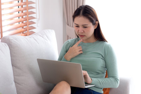 Young asian business woman working with laptop while thoughtful sitting on sofa in home office, businesswoman using on notebook in living room at home, woman thinking idea using laptop.の写真素材