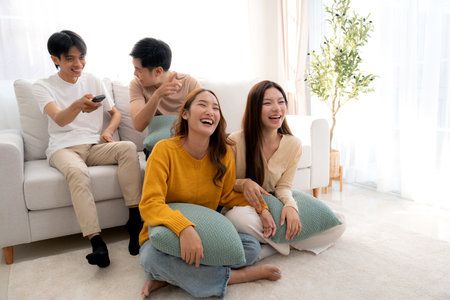 Group young asian friends watching TV together in a cozy living room at home with happy, laughing and enjoying sitting on sofa for watching television with relax, lifestyle and entertainment.の写真素材